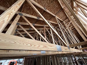 Interior of a wooden attic with exposed roof trusses and framing members down the slope of the ceiling area?