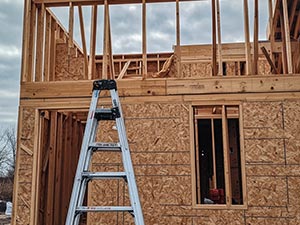 Construction site: wooden framing of a house with a metal ladder leaning against the wall in front of the frame.